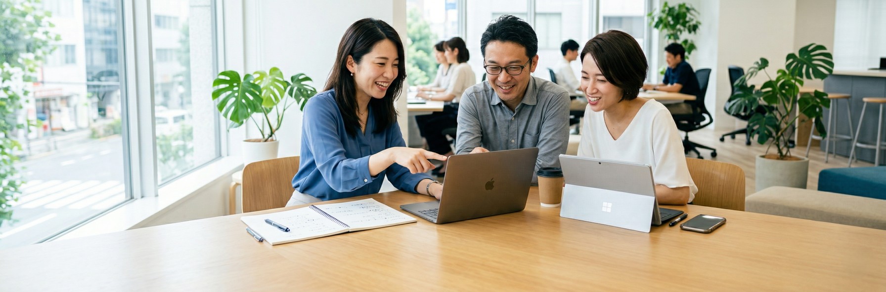 3人のビジネスパーソンがノートPCを囲んで笑顔でディスカッション